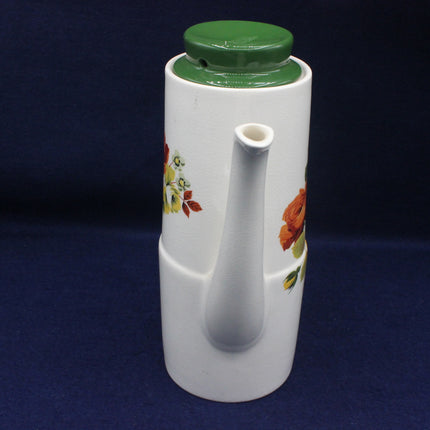 White ceramic oil dispenser with floral designs and green lid on a dark background