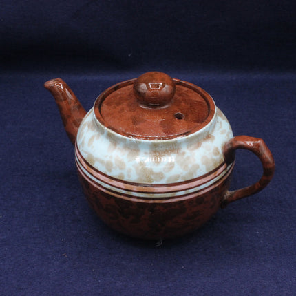 Ceramic teapot with brown and white speckled design on a dark blue background