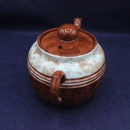 Ceramic teapot with brown lid and handle on a dark blue background