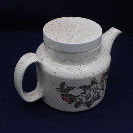 Speckled ceramic teapot with floral design on a dark background
