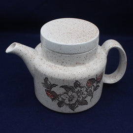 Speckled white ceramic teapot with floral design on a dark background