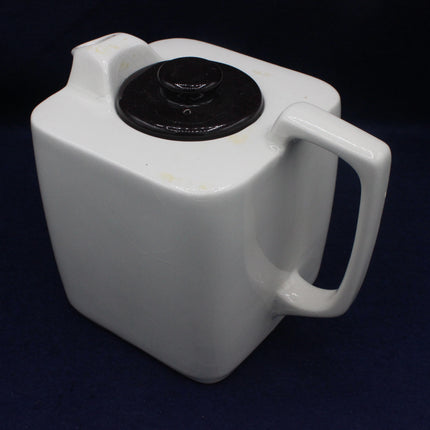 White ceramic container with black circular lid on a dark background