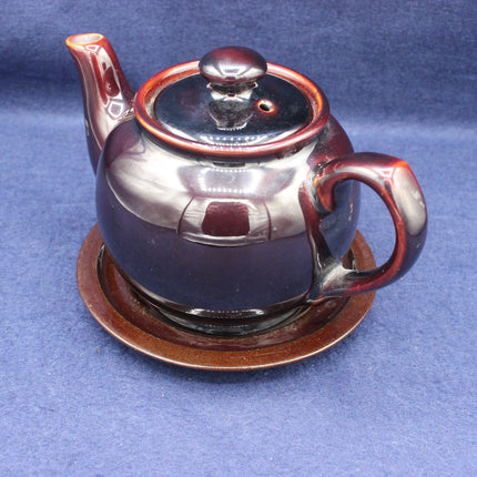 Ceramic teapot with a lid on a matching saucer against a blue background