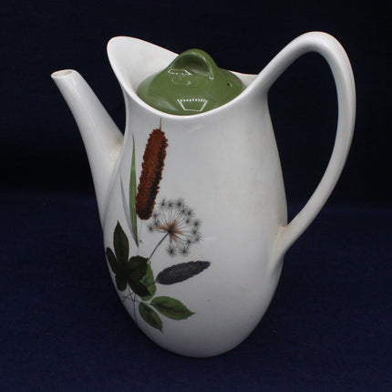 White ceramic teapot with botanical designs on a dark background