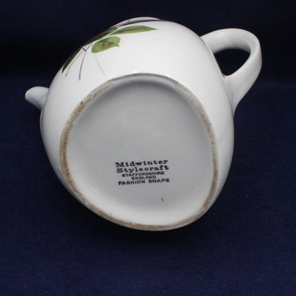 White ceramic teapot with green leaf design on a dark blue background