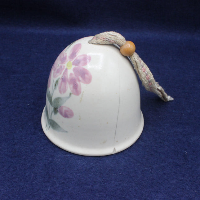 White ceramic bell with floral design and string on a blue background