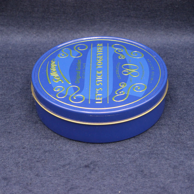 Blue round tin with gold text on a dark gray background