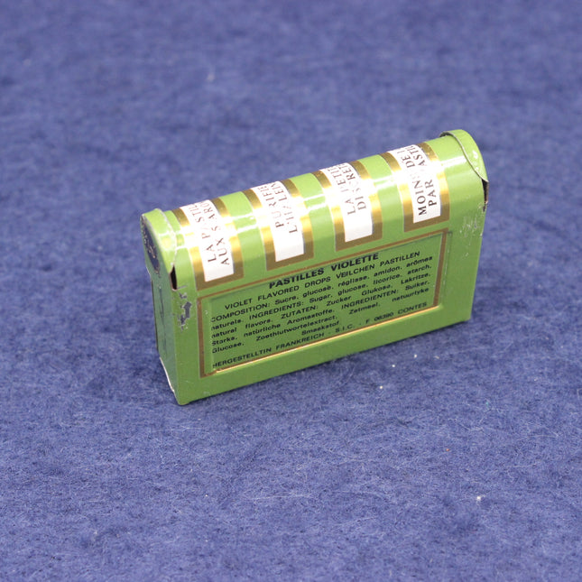 Green tin sweet box with multiple labels on a blue textured background