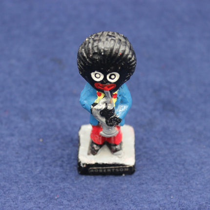 Small figurine of a Golly character with a black top hat and red shoes on a blue background