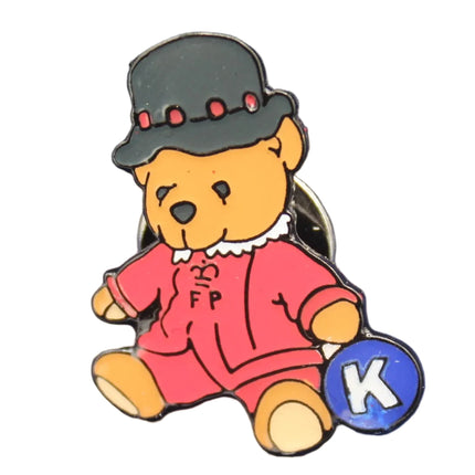 Teddy bear pin with a top hat and red outfit on a textured blue background