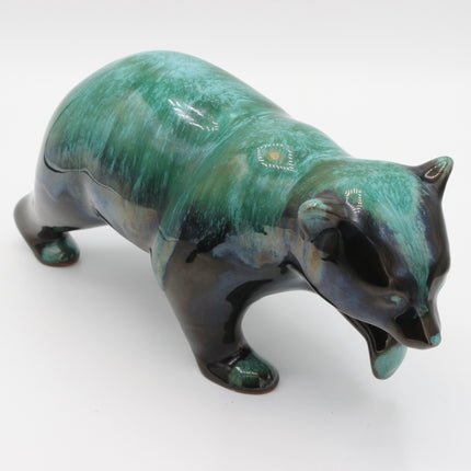 A ceramic bear figurine with a glossy green and black glaze, featuring hand-painted white and yellow details on its back and head, set against a plain white background.