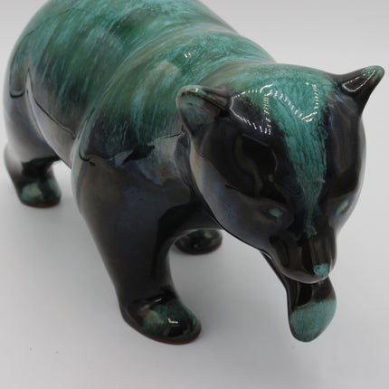 A glossy ceramic figurine of a bear, featuring a textured teal and black glaze, photographed on a neutral light gray background.