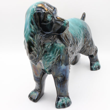 A ceramic figurine of a Cocker Spaniel dog with a glossy glaze featuring teal, turquoise, and black colors, set against a plain white background.