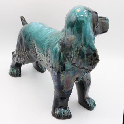 A glazed ceramic dog figurine with a glossy teal, green, and black marbled finish, standing on a white background.