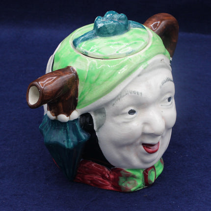 Ceramic teapot shaped like a face with a green hat and smoking pipe on a blue background