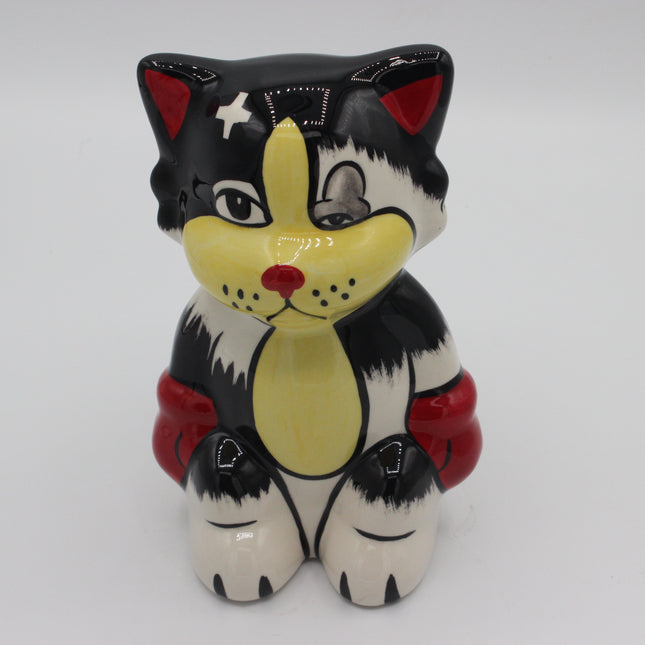 A ceramic cat figurine with a black, white, and yellow color scheme, featuring a red nose, red inner ears, and red cuffs, shown against a plain light gray background.