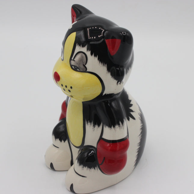 A ceramic cat figurine or piggy bank painted in a stylized black, white, yellow, and red design, photographed on a plain light gray background.