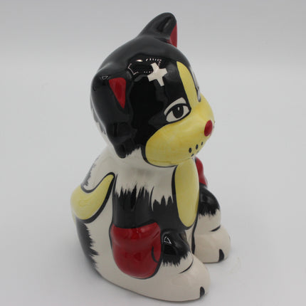 A glossy ceramic cat figurine in a stylized black, white, and yellow color scheme with red accents, photographed on a seamless light gray background.