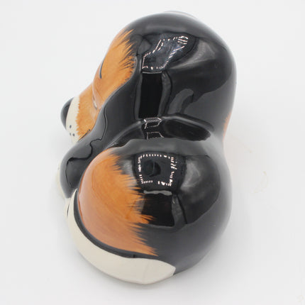 A glossy ceramic dog-shaped bowl or container, shown from a high-angle back view. The design features a black body with orange and white painted fur details, resembling a corgi or similar dog breed.