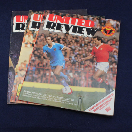 Three Manchester United Review football match programs on a dark background