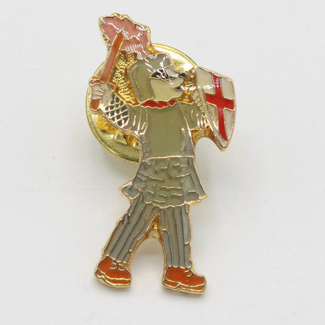 A vintage-style enamel pin depicting a knight in gold armor holding a red sword and shield with a red cross, set against a plain white background.