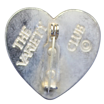 Heart-shaped metal object with 'The Vault Club' engraving on a blue textured background