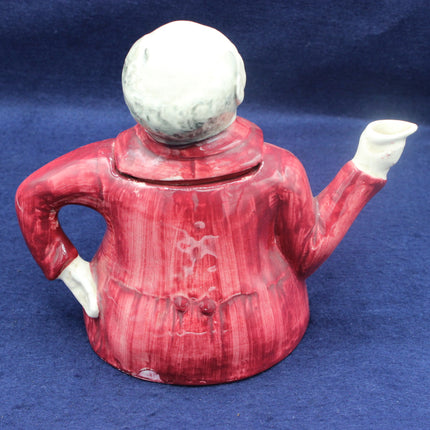Red ceramic teapot with a white face on a blue background