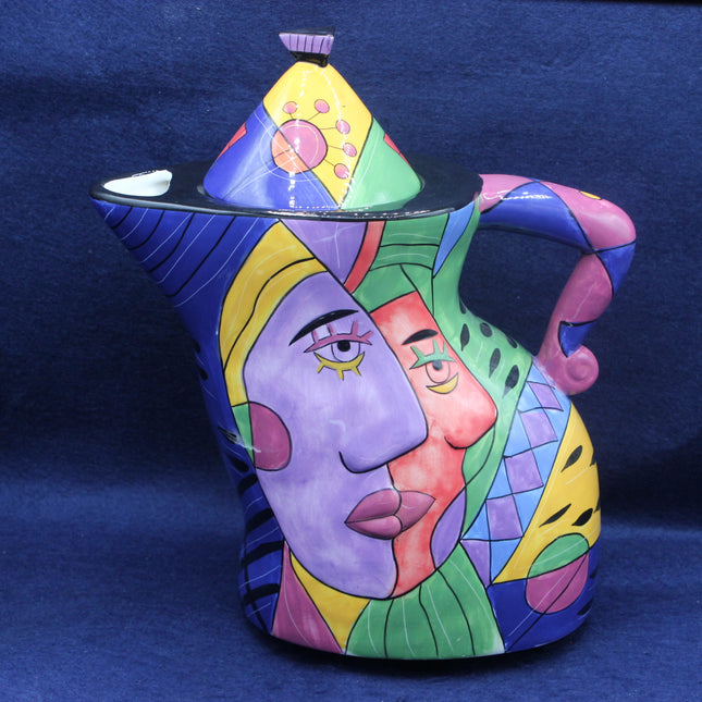 Colorful ceramic teapot with artistic face design on a blue background