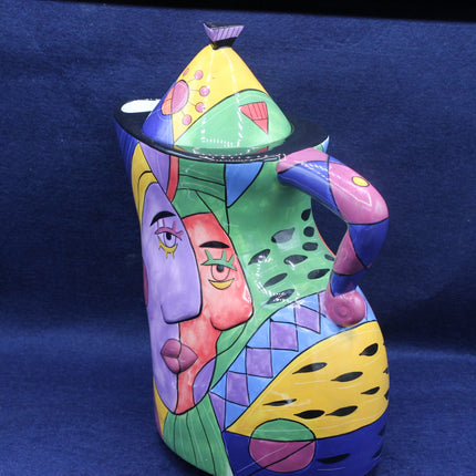 Colorful ceramic pitcher with abstract face design on a blue background