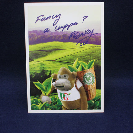 Card with a cartoon monkey holding a basket of tea leaves and text 'Fancy a cuppa? Monkey' on a scenic background.