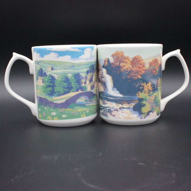 Two mugs with scenic designs on a dark background