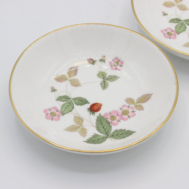 A white ceramic bowl with a delicate gold rim and a hand-painted strawberry and pink flower pattern, shown on a clean white background with another bowl partially visible in the upper right.