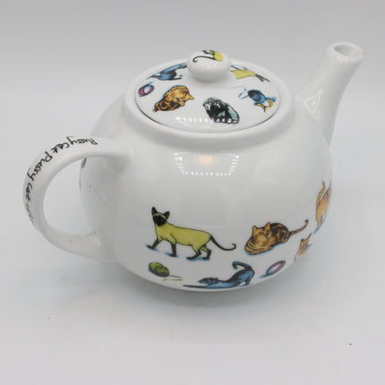 A white ceramic teapot decorated with colorful illustrations of various cats in different poses, along with black handwritten text on the handle, set against a plain light gray background.
