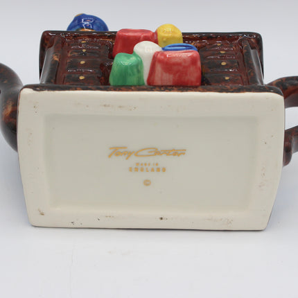 A vintage ceramic tea or coffee pot shown from the bottom, featuring a cream-colored glazed base with gold 'Paul Cardew' and 'Made in England' branding, and a brown handle with colorful glazed accents.