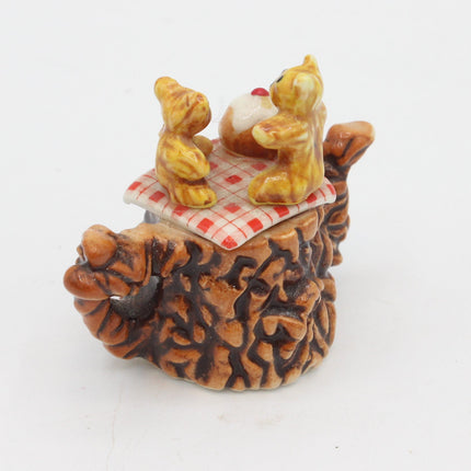 A small decorative figurine of two yellow teddy bears sitting on a red-and-white checkered blanket atop a brown acorn-shaped base, photographed against a plain white background.