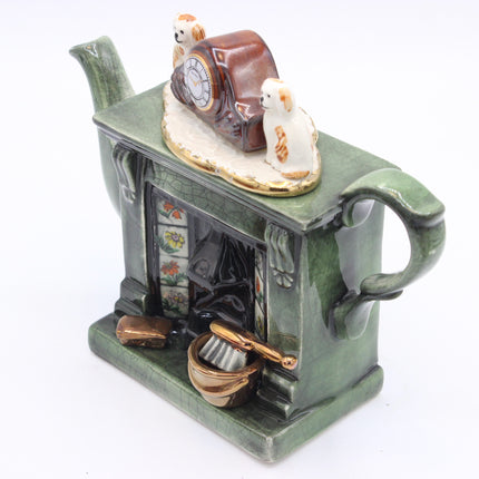 A vintage-style green ceramic teapot-shaped container with a fireplace facade, featuring a brown and white clock figurine and two small white dogs with gold markings on top, set against a plain white background.