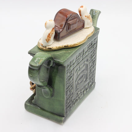A vintage green ceramic tea towel holder or decorative container with a small brown house and two white dogs figurine on top, photographed on a white background.