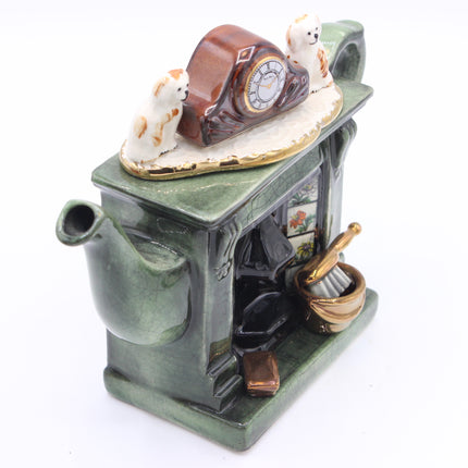 A ceramic teapot-shaped clock and candle holder with a green glazed body, featuring a brown clock on top with two white cats, a lit candle in a basket, and a small window panel.
