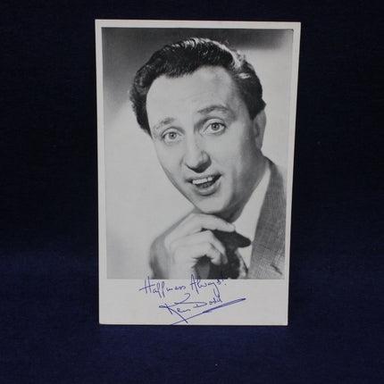 Black and white photo of a Ken Dodd with a signature below on a dark background