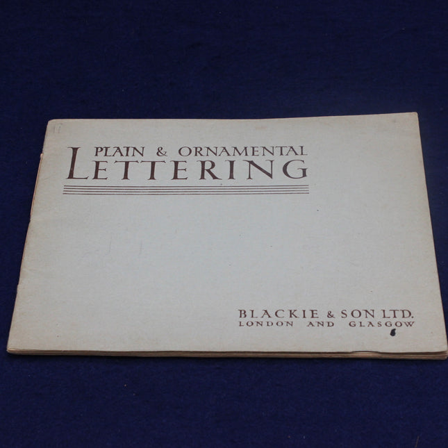 Book titled 'Plain & Ornamental Lettering' by Blackie & Son Ltd on a dark blue background