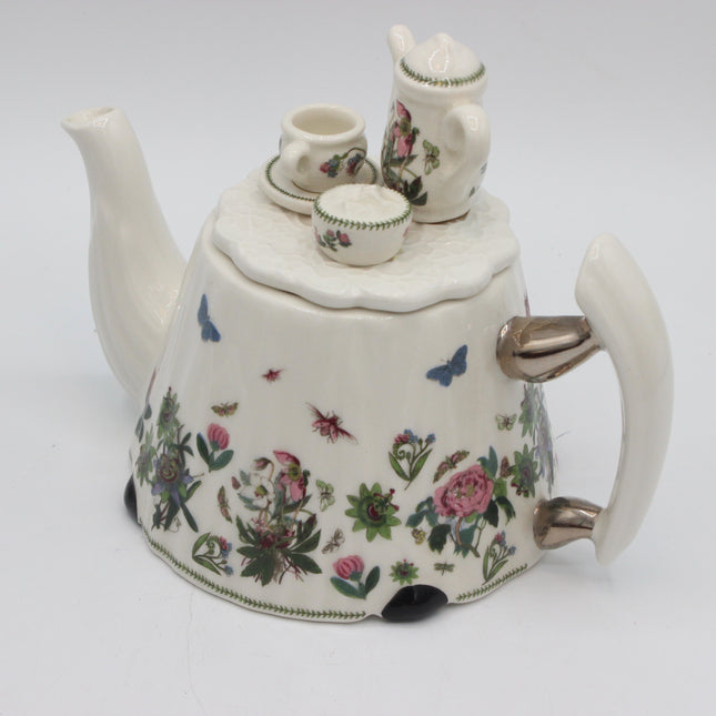 A vintage white porcelain teapot with a floral and butterfly pattern, featuring a matching small teapot and cup set on top, photographed against a plain white background.