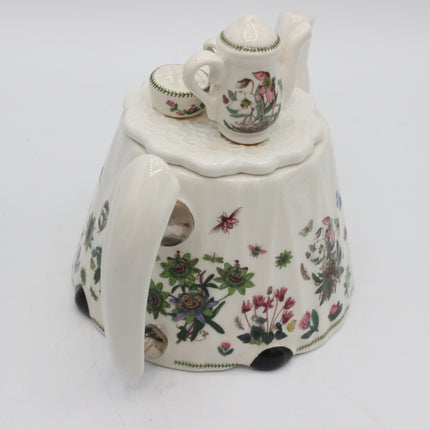 A vintage white porcelain teapot with a lid, accompanied by a small matching cup and saucer, decorated with colorful floral and butterfly motifs on a white background.