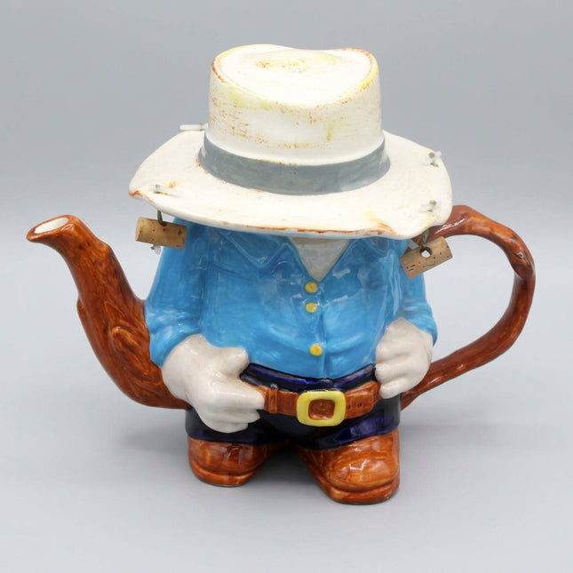 Teapot shaped like a Aussie figure with a blue shirt and white hat on a dark blue background
