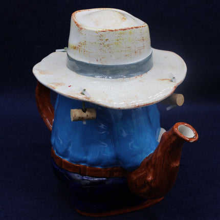 Ceramic Aussie figurine with a blue body, white hat, and brown pants on a dark background