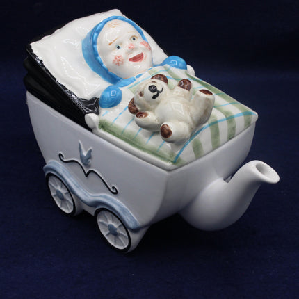 Ceramic teapot shaped like a baby carriage with a baby and dog figure on a dark background