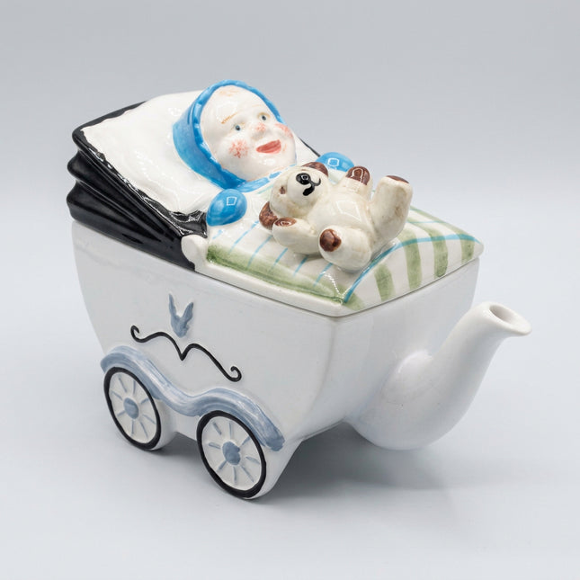 Ceramic teapot shaped like a baby carriage with a baby and dog figure on a dark background