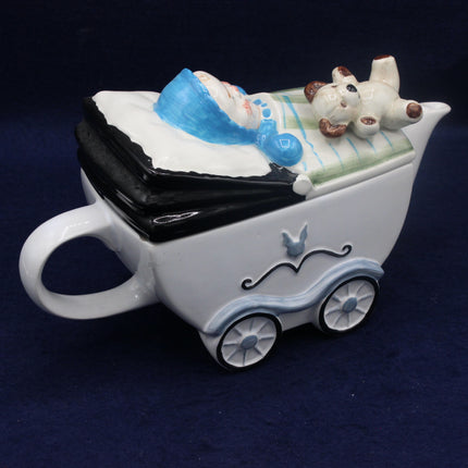 Ceramic baby carriage mug with baby and dog figurines on a dark blue background