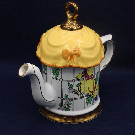 Decorative teapot with yellow lid featuring a bird in a cage design on a dark background