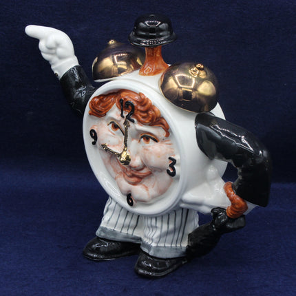 Decorative tea pot of a man with a clock face, wearing a hat and gloves, on a dark blue background.