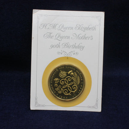 Gold coin on a card with text about Queen Elizabeth's Mothers 90th birthday, against a dark background.
